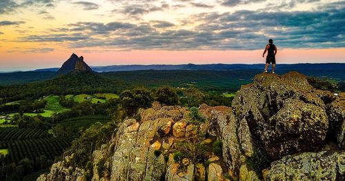 Rear view of man standing on rock formation against sky during sunset