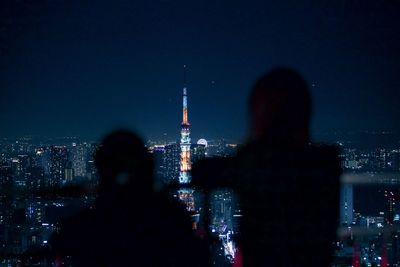 Rear view of illuminated cityscape against sky at night