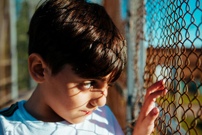 Close-up portrait of boy looking through fence