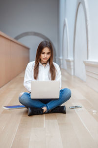 Young woman with long hair using laptop while sitting on floor