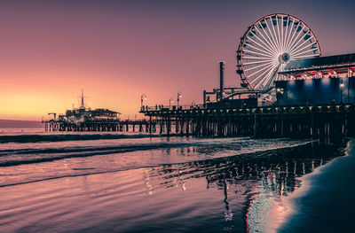 View of ferris wheel in sea at sunset