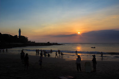 Silhouette people on beach against sky during sunset