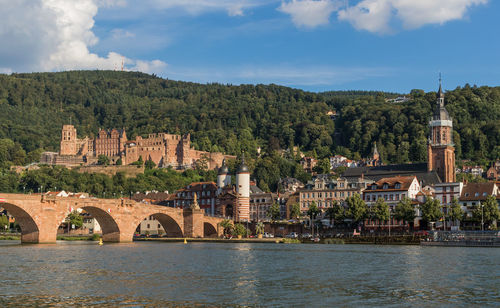 Arch bridge over river by buildings against sky