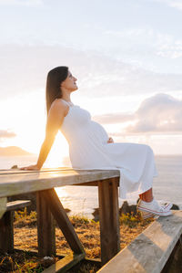 Woman sitting on seat by sea against sky