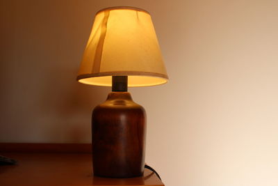 Close-up of illuminated lamp on table against wall at home