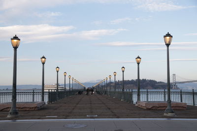 Street light on footpath by sea against sky