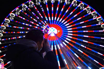 Low angle view of man photographing illuminated ferries wheel at night