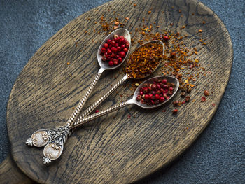 Close-up of chili flakes and dried fruits in spoons on wooden cutting board