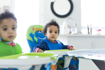 Portrait of baby girls sitting on high chairs at home