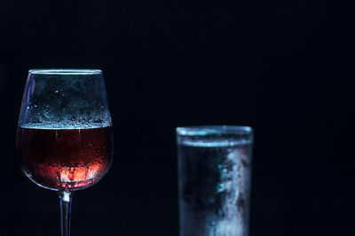 Close-up of wine glass against water glass and black background