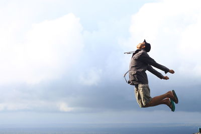 Side view of young man jumping against cloudy sky