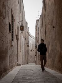 Rear view of man standing on footpath amidst buildings