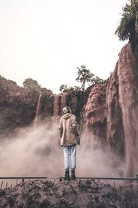 Rear view of man standing by waterfall against sky