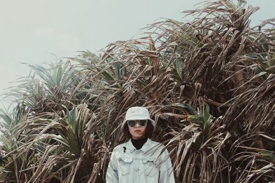 Portrait of young woman standing by palm tree against sky