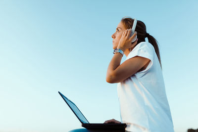 Low angle view of woman using smart phone against clear sky