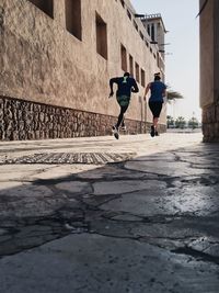 Low angle view of man and woman jogging on pathway during sunny day