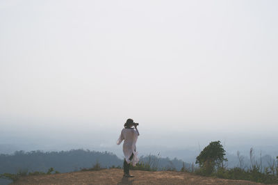 Full length of woman photographing on hill against clear sky during sunny day