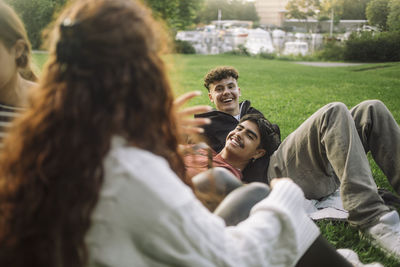 Smiling male friends talking with female friends while lying down at park