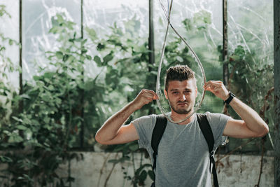 Portrait of young man holding rope standing against plants