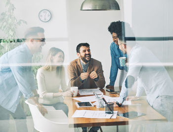 Smiling business colleagues discussing in office seen through glass