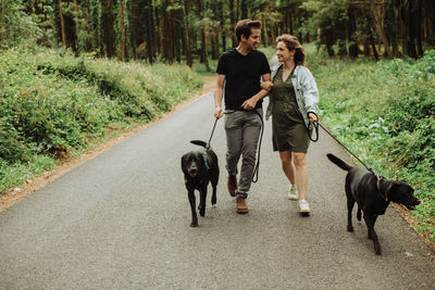 Couple looking at each other while walking dogs on leash in the forest