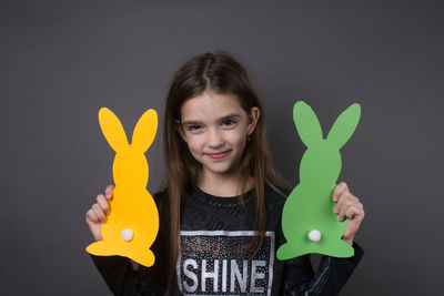 Portrait of smiling girl holding paper eater bunny against gray background