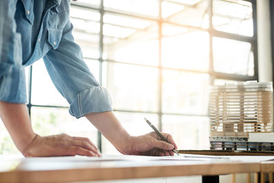 Midsection of architect drawing blueprint while working in office