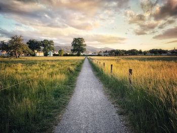 Dirt road amidst field against sky