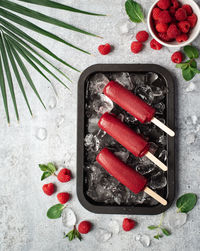 Raspberry popsicles on a tray with ice and fruit on grey background.