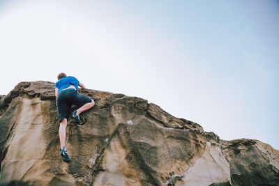 Man climbing on rock formation against sky