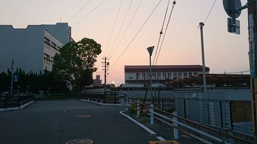 Road by buildings against sky during sunset