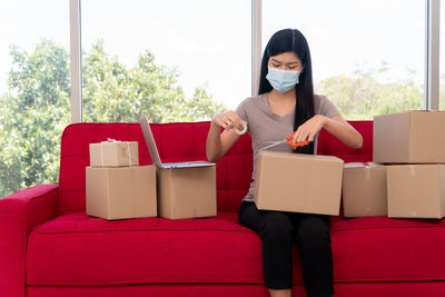 Young woman with mask packaging while sitting on sofa