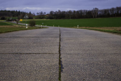 Surface level of street amidst field against sky