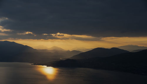 Scenic view of lake by silhouette mountains against sky during sunset