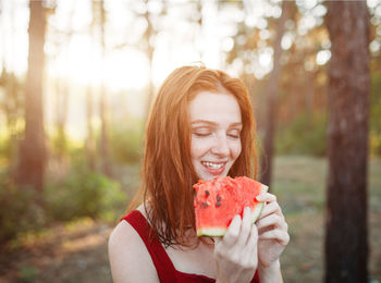 Close-up of smiling woman with eyes closed eating melon in forest