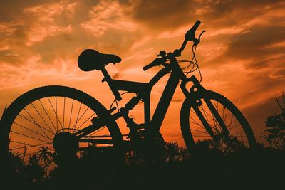 Silhouette of bicycle on field against orange sky