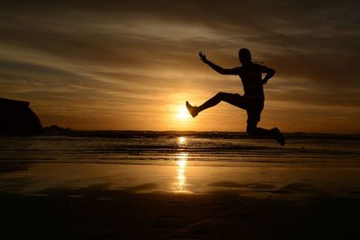 Silhouette man jumping on beach against sky during sunset