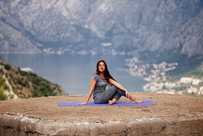 Portrait of young woman exercising on cliff against mountain