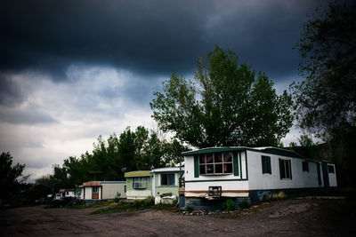 Trailer home by trees against cloudy sky