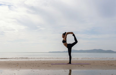 Full length of woman performing yoga on beach against sky