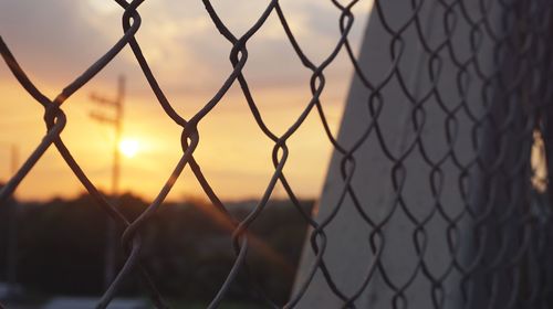 Close-up of chainlink fence against sunset sky