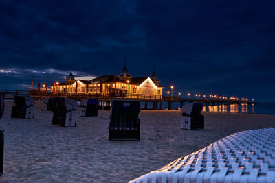 Illuminated building by sea against sky at dusk