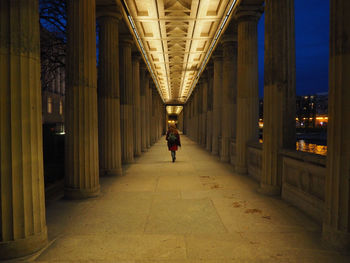 Full length rear view of woman walking in illuminated passage at night