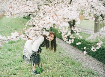 Full length portrait of woman bending by flowering tree at park