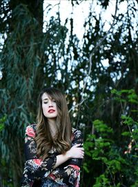 Beautiful woman standing with arms crossed against trees