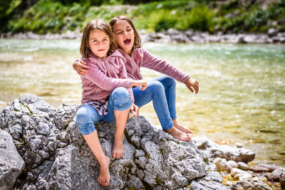 Portrait of sisters sitting on rock against lake