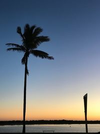 Silhouette palm tree by sea against clear sky at sunset