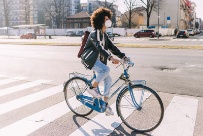 Young woman with face mask and backpack riding bicycle in city