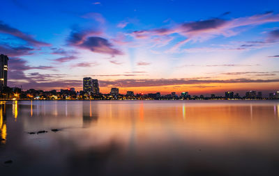 Scenic view of lake by buildings against sky during sunset