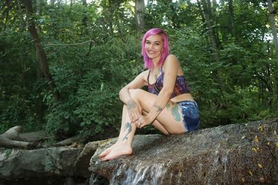 Portrait of seductive woman with dyed hair sitting on rock in forest